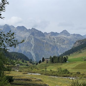 Weitläufige alpine Landschaft mit grünem Vordergrund und majestätischen, bewölkten Berggipfeln.